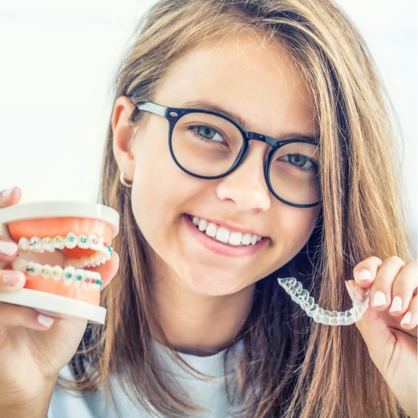 Young girl smiling while holding invisalign and braces